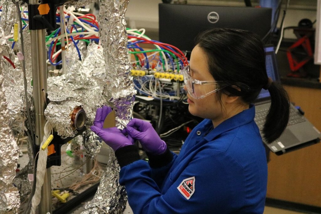 Researcher holds a silicon wafer in tweezers in front of a scientific device.