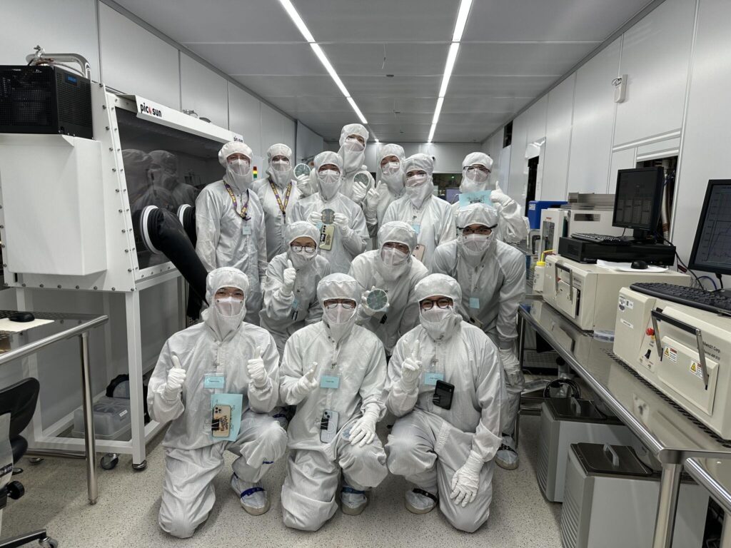 Group of people gathered for a group photo in a lab in full clean room protective gear