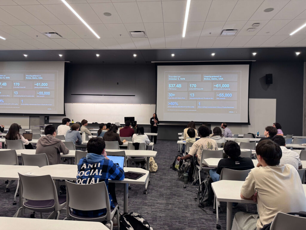 Large group of students in a lecture hall facing projection screens.